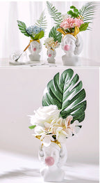 White resin girl-head vases featuring gold headbands and pink bubblegum spheres, filled with artificial flower bouquets.