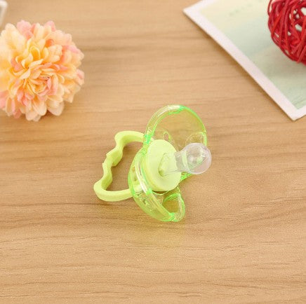 Translucent green baby pacifier with round silicone nipple and handle, set against a wooden surface.