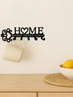 Black metal wall hook rack with "HOME" text, a heart design, and five hooks, hanging a beige mug against a white wall.