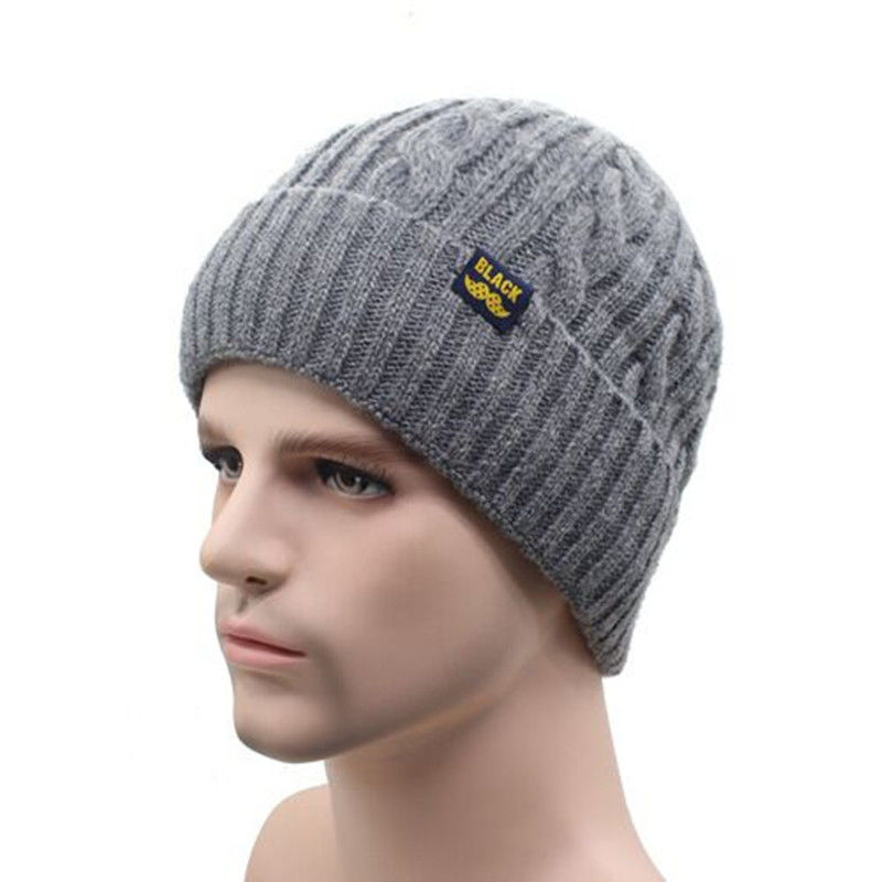 Grey cable-knit beanie on a mannequin head, featuring a ribbed cuff and a small square label reading "BLACK".