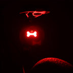 A bone-shaped red LED bicycle taillight glows brightly in the dark, mounted under a bike seat.