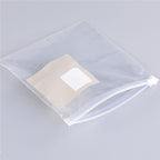 Empty, clear plastic zip-lock storage bag with a white adhesive square label on a grey background.