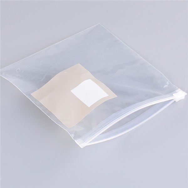 Empty, clear plastic zip-lock storage bag with a white adhesive square label on a grey background.