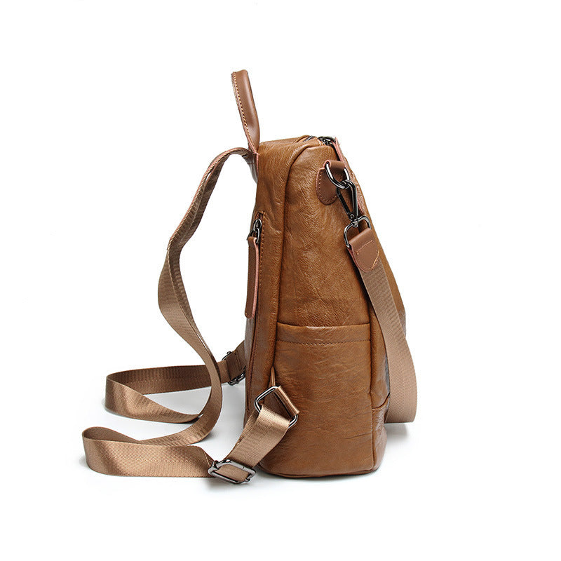 Side view of a brown soft leather convertible backpack with adjustable nylon straps and metal hardware on white.