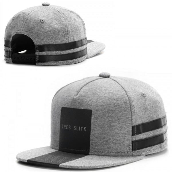 Grey heather baseball cap featuring a black rectangular front patch with "TRÈS SLICK" and two black side stripes.