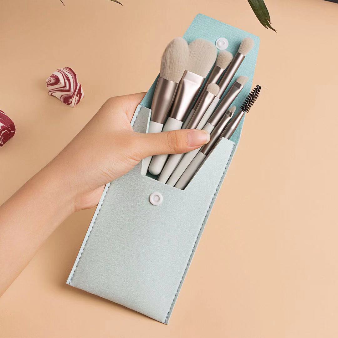Hand holding a light blue, snap-button vegan leather travel case filled with eight matching mini makeup brushes.