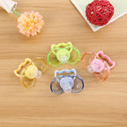 Four colorful, transparent plastic baby pacifiers with round nipples arranged on a wooden surface.