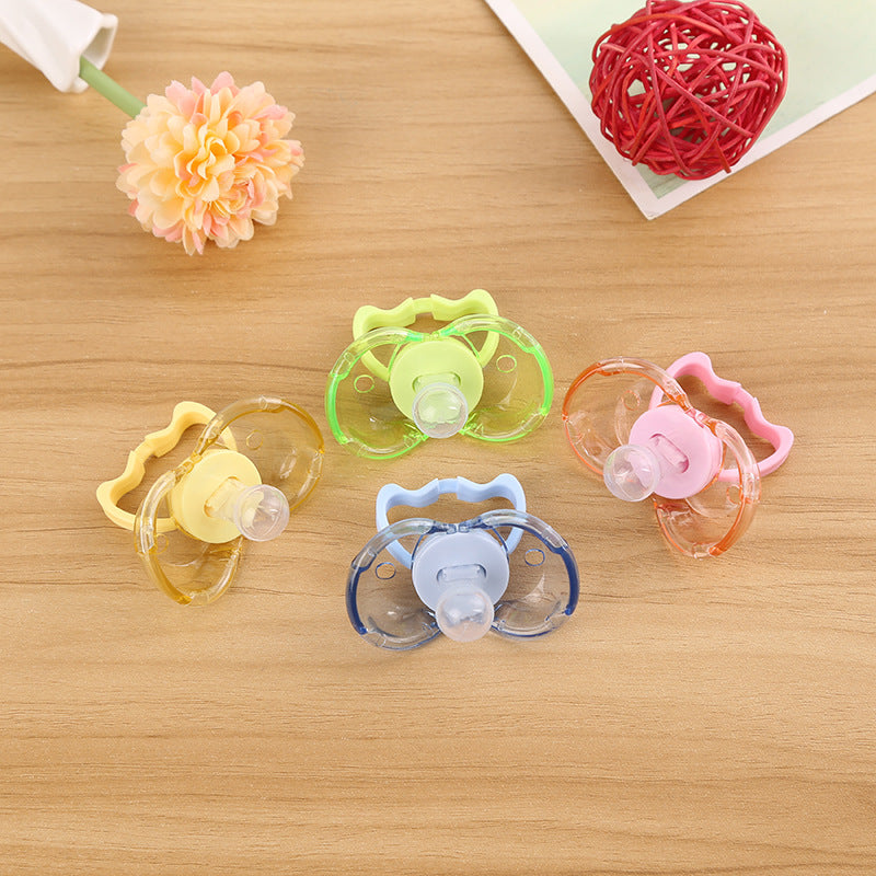 Four colorful, transparent plastic baby pacifiers with round nipples arranged on a wooden surface.
