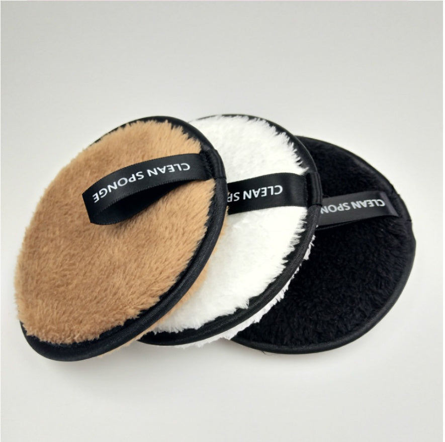 Three round, fuzzy, brown, white, and black cleansing makeup remover pads with black "CLEAN SPONGE" ribbon loops.