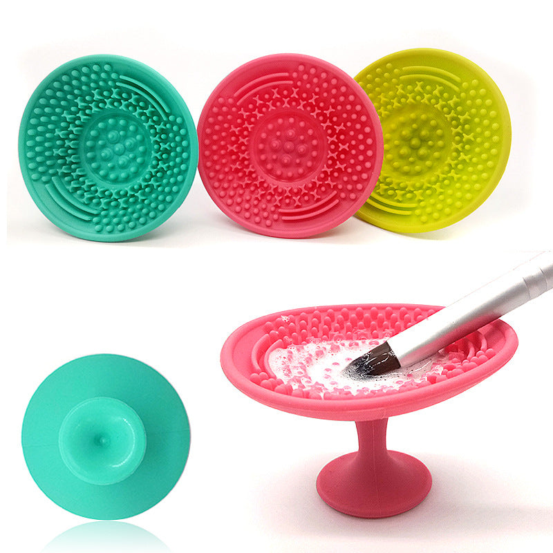 Teal, pink, and lime silicone makeup brush cleaning pads with textured scrubbing surfaces and rear suction cups.