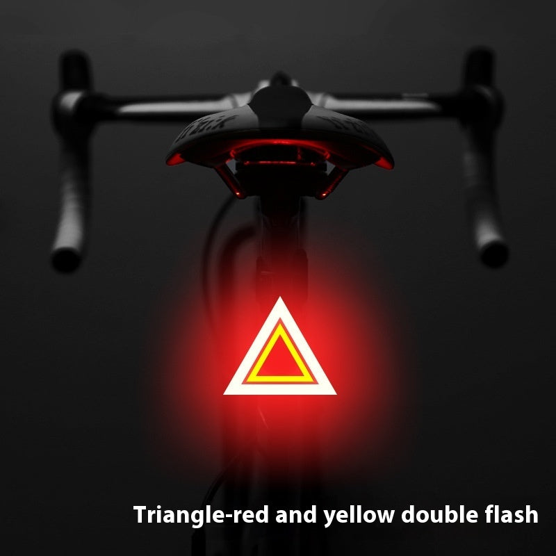 A triangular USB bicycle taillight glowing red and yellow, mounted on a bike seat against a dark background.