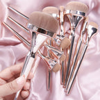 Drunk Gold makeup brush set with metallic rose-gold handles and soft, tan bristles on a draped pink satin background.