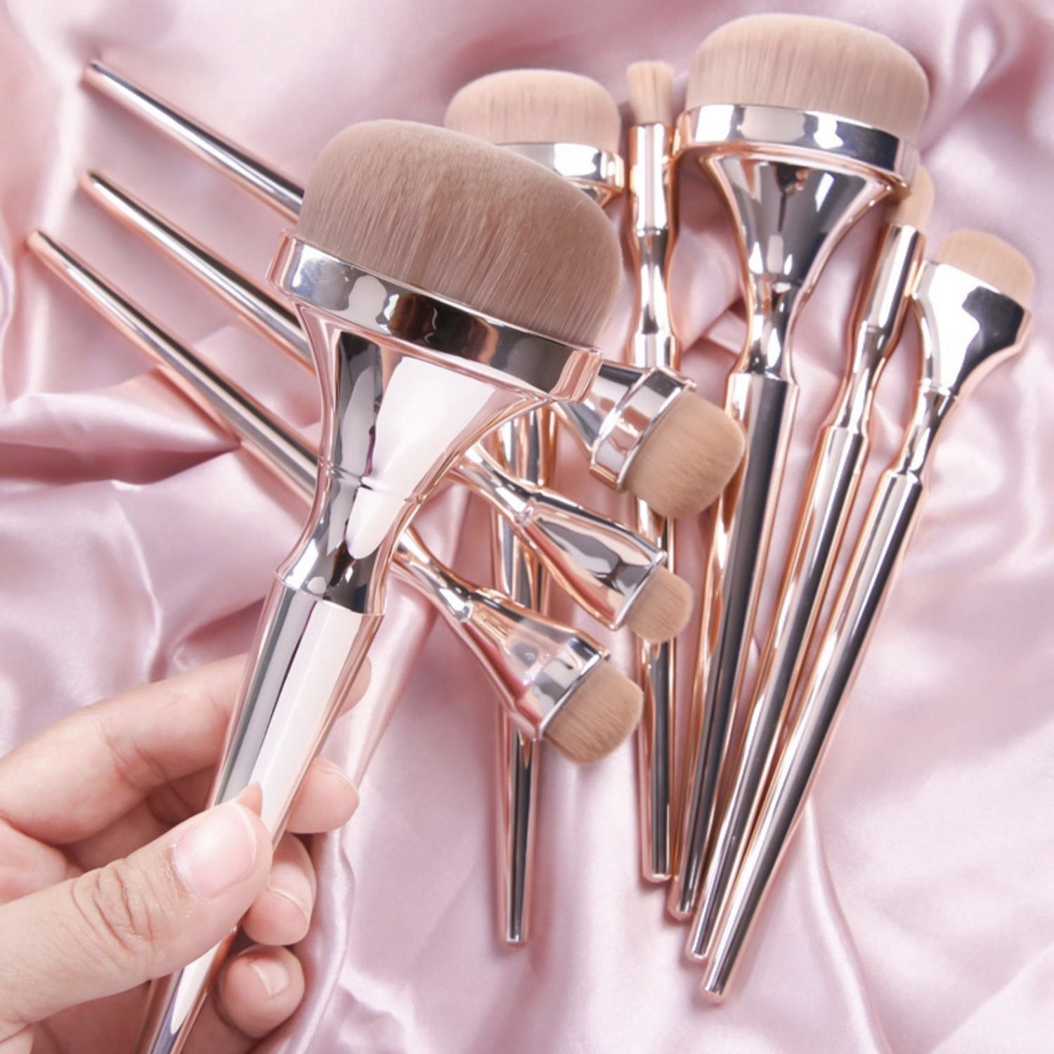 Drunk Gold makeup brush set with metallic rose-gold handles and soft, tan bristles on a draped pink satin background.