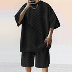 Model wears a black, loose-fit shorts set with a textured, jacquard plaid pattern and short sleeves.