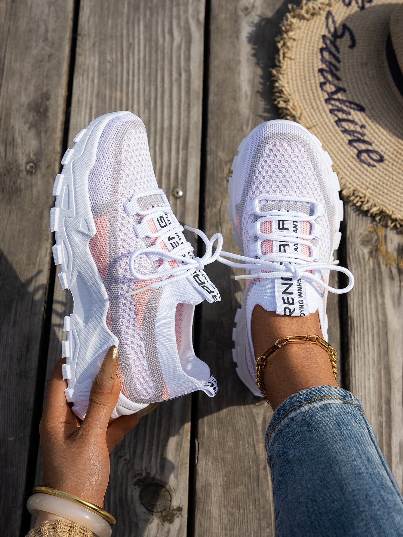 White, pink, and grey knit mesh lace-up sneakers with thick, chunky white rubber soles on a wooden dock.