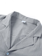 Close-up of a grey short-sleeve button-down shirt with a notched collar, featuring a textured linen-like fabric.