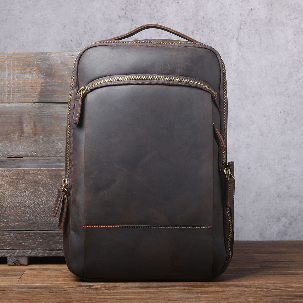 Vintage-style dark brown leather backpack with multiple brass-toned zippers and a top handle on a rustic backdrop.
