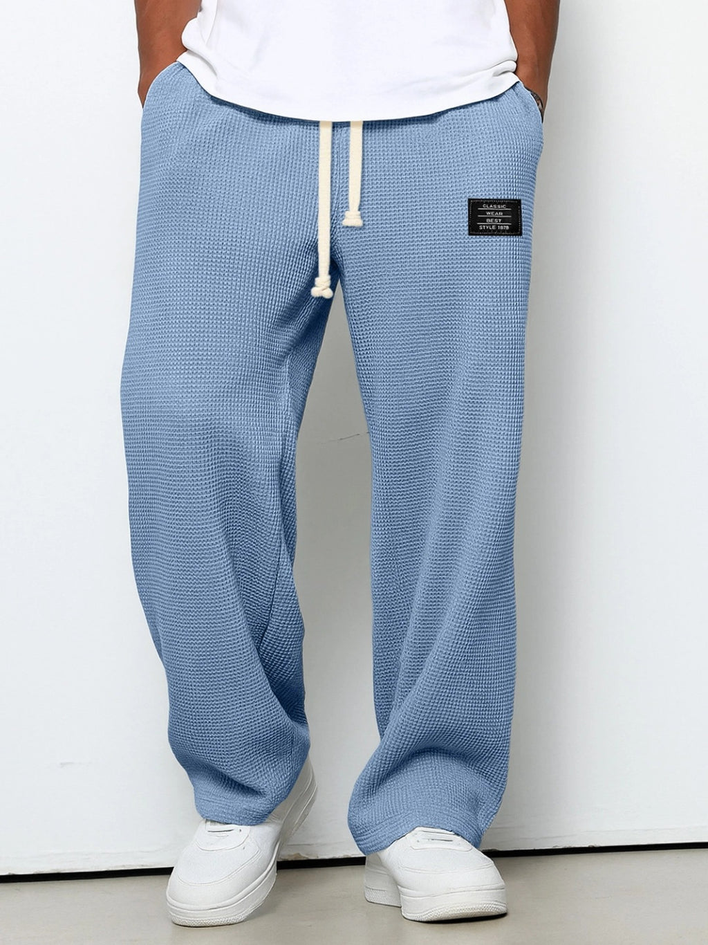 Loose blue waffle-knit casual trousers with a drawstring waist and a small rectangular patch on the upper thigh.