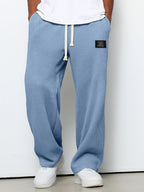 Loose blue waffle-knit casual trousers with a drawstring waist and a small rectangular patch on the upper thigh.