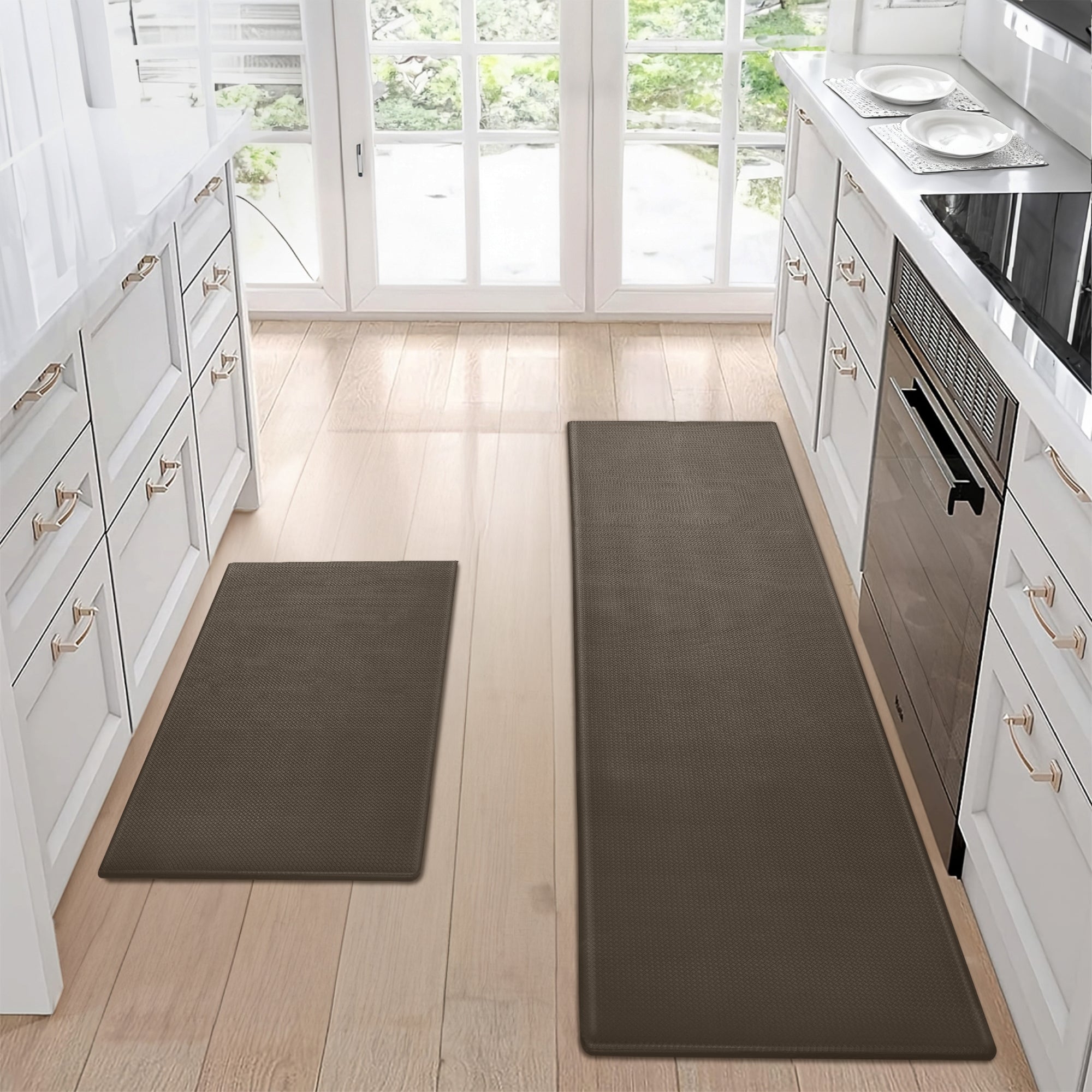 Two dark brown, waterproof kitchen mats on a light wood floor between white cabinets. Non-slip, easy-clean design.
