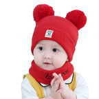 Baby wearing a red wool beanie with two pom-poms and a matching "love more" neck warmer on a white background.