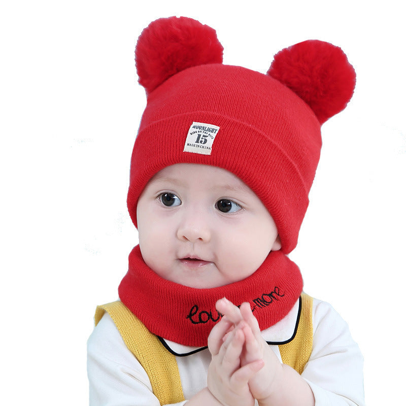 Baby wearing a red wool beanie with two pom-poms and a matching "love more" neck warmer on a white background.