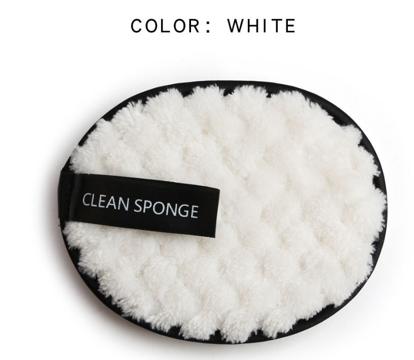 A white, fuzzy, round makeup cleansing sponge with a black trim and a black tag that reads "CLEAN SPONGE."
