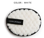 A white, fuzzy, round makeup cleansing sponge with a black trim and a black tag that reads "CLEAN SPONGE."