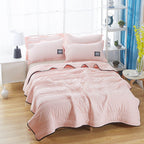 Soft pink cooling summer quilt set with quilted texture, matching pillows, and black-trimmed edges on a made bed.