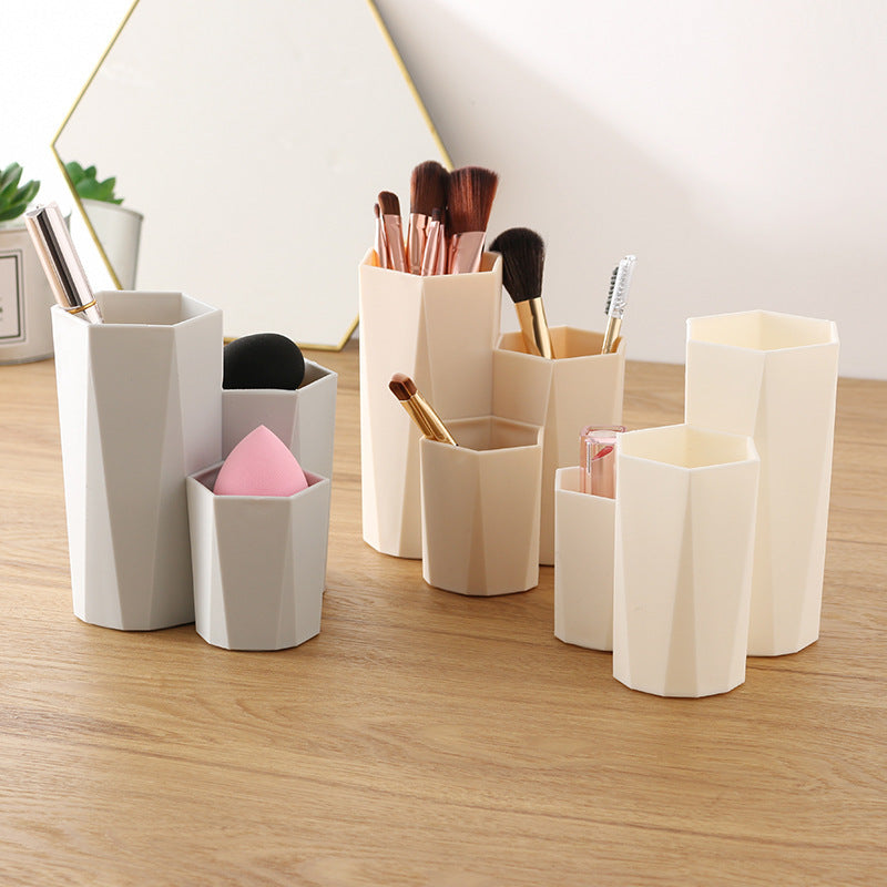 Grey and beige hexagonal plastic makeup brush holders on a wooden desk, holding brushes and sponges.