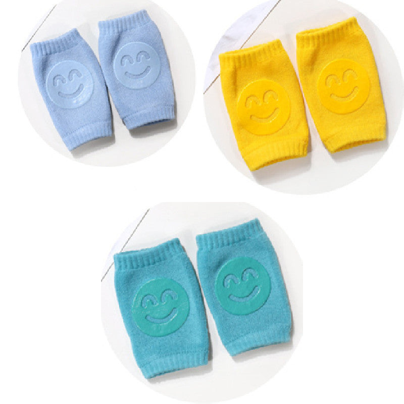Three pairs of soft terry baby knee pads in blue, yellow, and teal, each with a centered silicone smiley face grip.