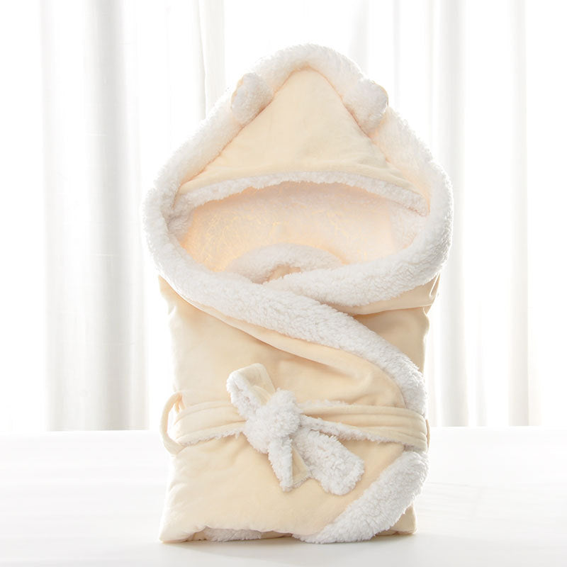 Cream-colored fleece baby swaddle with white plush trim, hood with ears, and a soft tie closure.