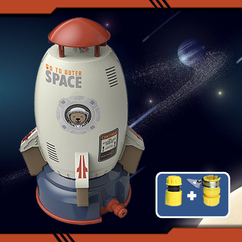 White rocket sprinkler toy with orange top, astronaut bear graphic, and blue base, includes yellow hose connectors.