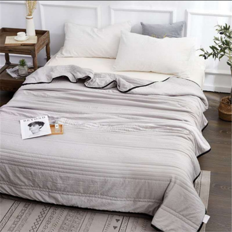 A soft, grey lightweight cooling summer quilt with black trim, draped neatly over a bed in a modern bedroom setting.