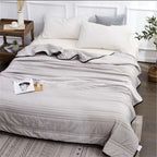 A soft, grey lightweight cooling summer quilt with black trim, draped neatly over a bed in a modern bedroom setting.