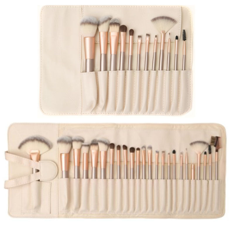 Set of 24 makeup brushes with champagne gold handles and synthetic white hair, stored in a cream-colored roll-up case.