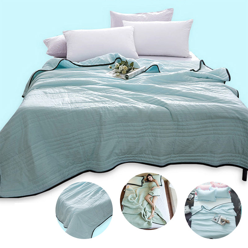 Light blue quilted summer cooling blanket with black trim, shown on a bed with white pillows and circular details.