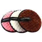 Three plush, round makeup puffs in pink, white, and brown with black "CLEAN SPONGE" finger straps.