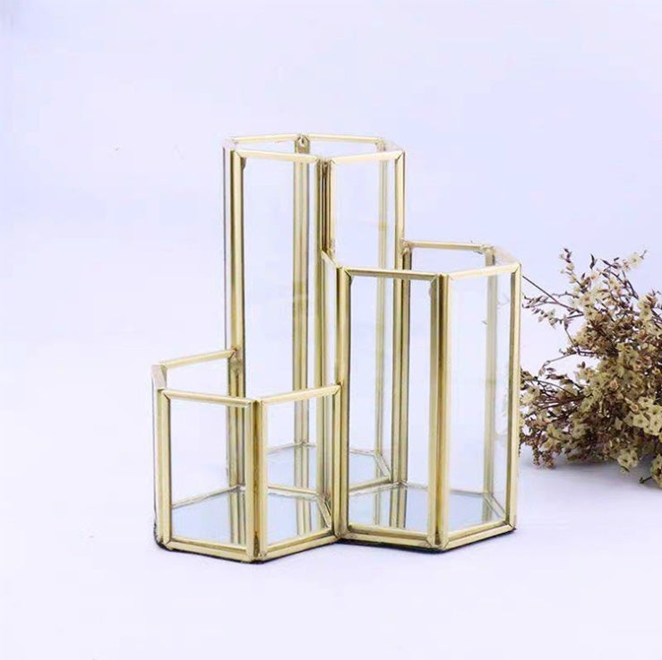 Gold-trimmed, hexagonal glass makeup brush holder with three tiered compartments. Minimalist, geometric design.