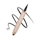 Black self-adhesive liquid eyeliner pen with gold, pearl, and rhinestone-encrusted barrel over a black ink swirl.