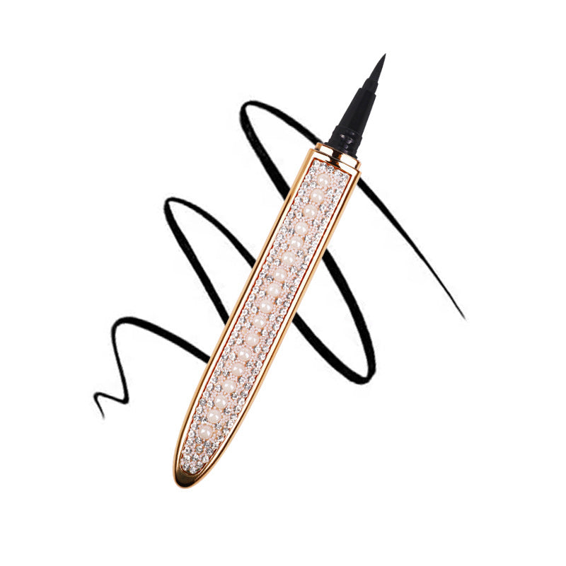 Black self-adhesive liquid eyeliner pen with gold, pearl, and rhinestone-encrusted barrel over a black ink swirl.