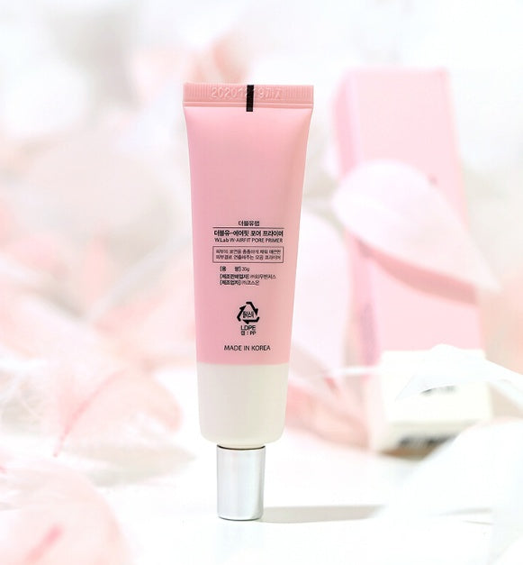 A pale pink tube of W.Lab Airfit Pore Primer stands upright against a soft, blurred pink background.