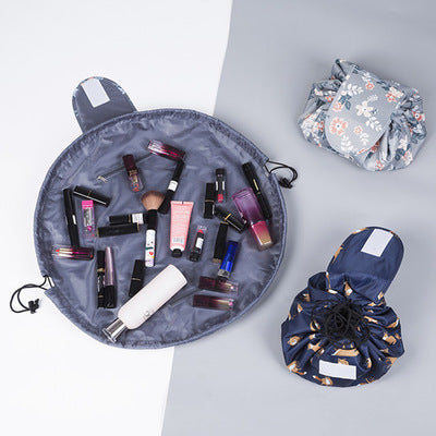 Three drawstring cosmetic bags, one open and two closed, featuring floral and patterned fabric in gray and navy.