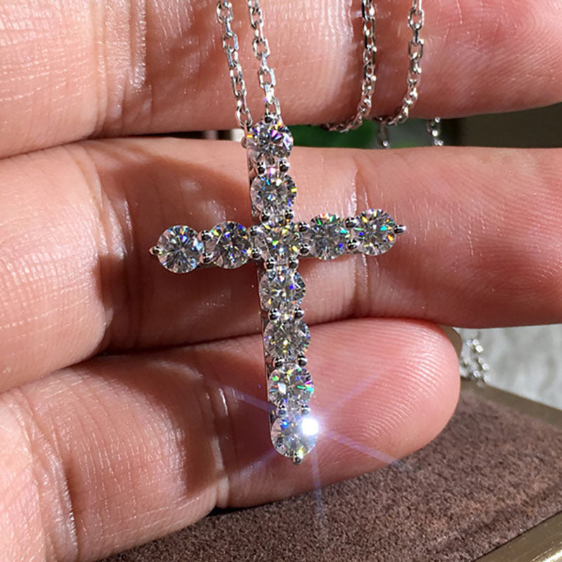 Silver cross necklace featuring sparkling round-cut crystals held in hand, set on a matching metallic chain.