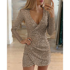 A woman wears a long-sleeve, V-neck gold sequin mini dress with a draped, irregular wrap-style skirt.