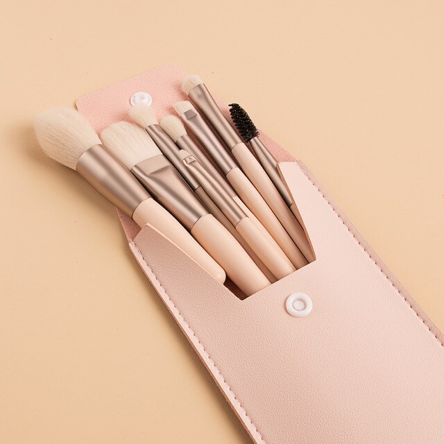 A portable set of 8 beige makeup brushes with metallic handles inside a soft pink leatherette snap-button pouch.