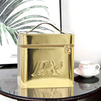 Metallic gold, rectangular portable makeup bag with top handle, zipper closure, and embossed logo on a glass table.