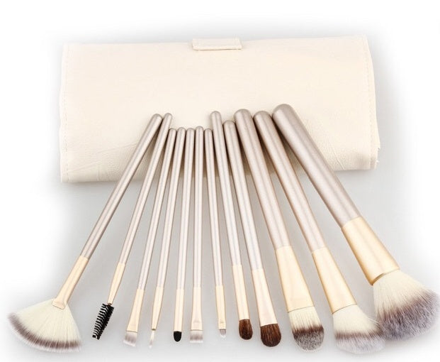 A set of 11 champagne-gold makeup brushes with white/brown bristles and a matching cream-colored roll-up case.