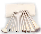 A set of 11 champagne-gold makeup brushes with white/brown bristles and a matching cream-colored roll-up case.