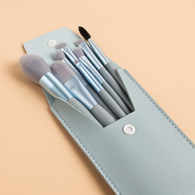 Portable makeup brush set with light blue leather case, grey bristles, and metallic light blue handles.